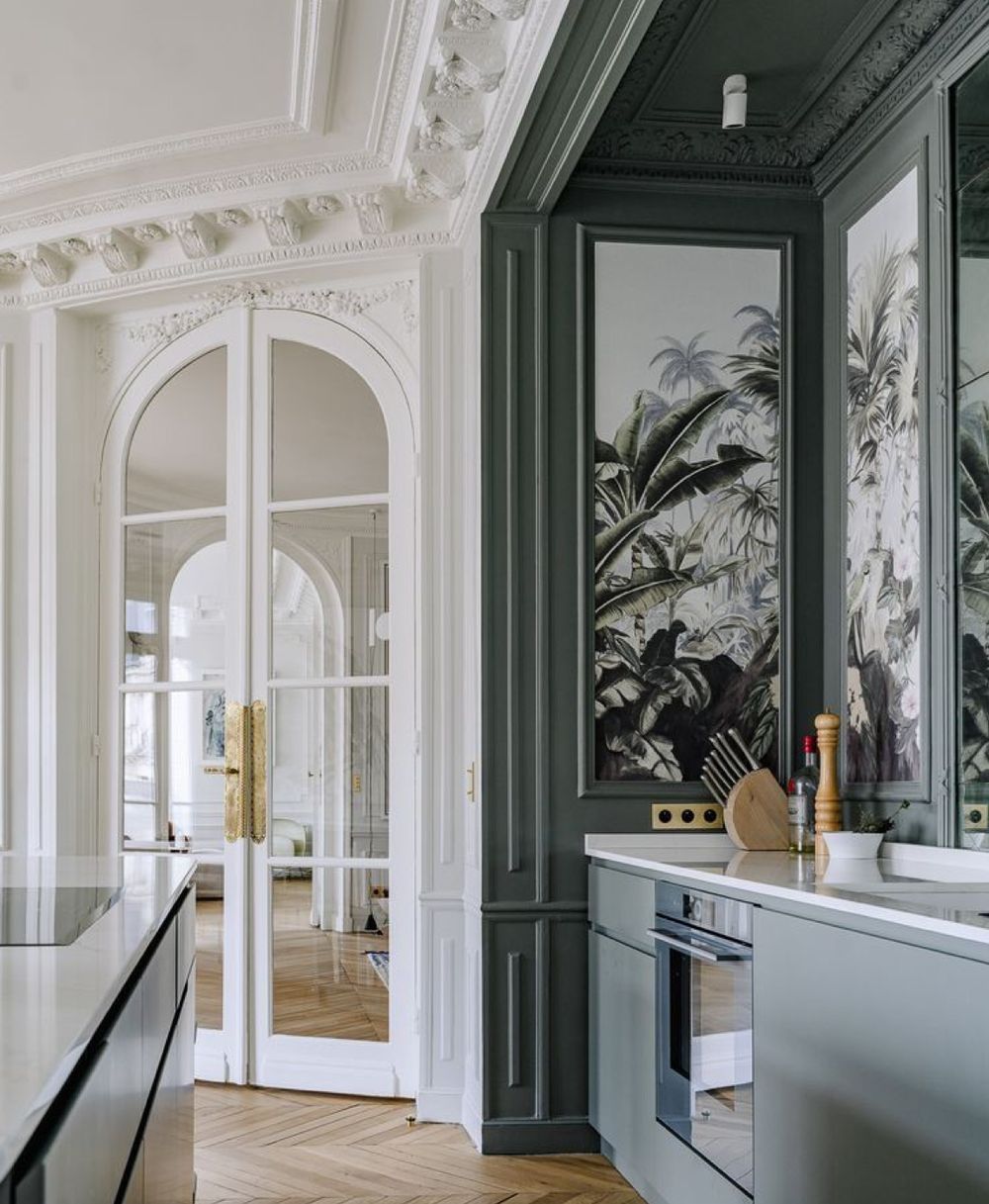 Cuisine avec moulures blanches au plafond, boiseries vert foncé et parquet en chevrons